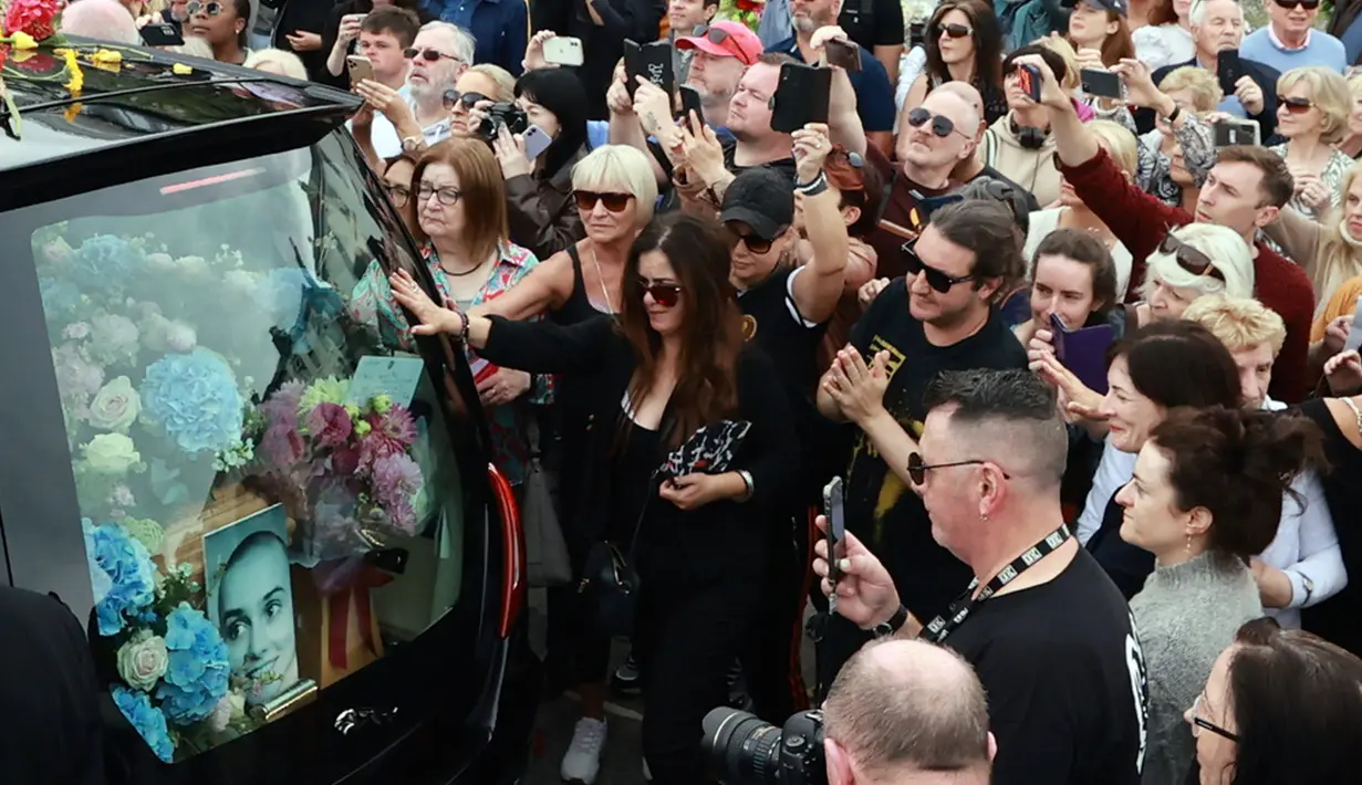 Memasuki siang hari, ribuan orang yang hadir semakin antusias saat melihat rombongan iring-iringan jenazah Sinead O’Connor telah tiba di rumah yang pernah ditinggali Sinead O’Connor selama 15 tahun. Rumah tersebut berada di kawasan tepi pantai Bray. (Liam McBurney/PA via AP)