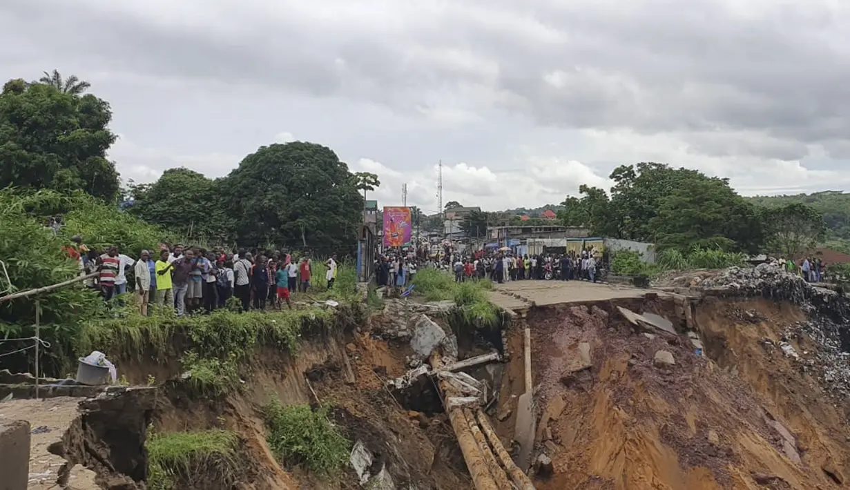 Warga melihat jalan ambruk oleh tanah longsor yang disebabkan hujan lebat melanda distrik Lemba, Kinshasa di Republik Demokratik Kongo pada Selasa (26/11/2019). Bencana tanah longsor ini juga telah melumpuhkan aktivitas warga dan lalu lintas. (AFP/Ange Kasongo)