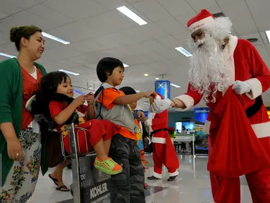 Santa Claus memberikan hadiah kepada anak-anak di Bandara Soekarno Hatta, Tangerang, Banten, Selasa (22/12). Sejumlah orang berkostum santa claus membagikan coklat kepada penumpang yang berada dibandara. (Liputan6.com/Faisal R Syam)