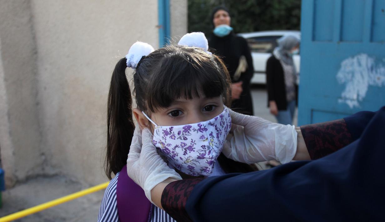 Seorang guru menyesuaikan posisi masker seorang pelajar di sekolah pada hari pertama tahun ajaran baru di kamp pengungsi Al-Amari di Kota Ramallah, Tepi Barat (6/9/2020). Pelajar Palestina memulai tahun ajaran baru setelah belajar di rumah selama enam bulan akibat Covid-19. (Xinhua/Nidal Eshtayeh)