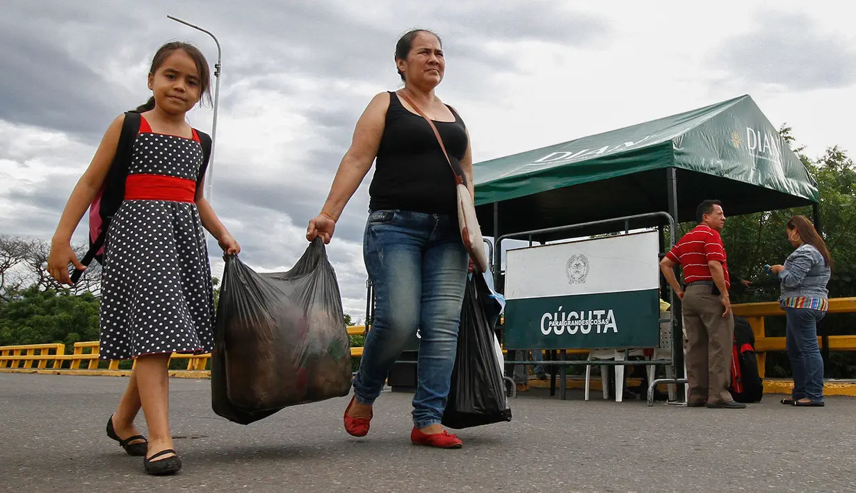 Seorang ibu dan anaknya membawa bahan makanan yang dibeli di Kolombia, berjalan pulang menuju perbatasan di kota Cucuta, Rabu (6/7). Sejumlah warga Venezuela mencari makanan dengan menerobos perbatasan masuk ke wilayah Kolombia. (Schneyder MENDOZA/AFP)