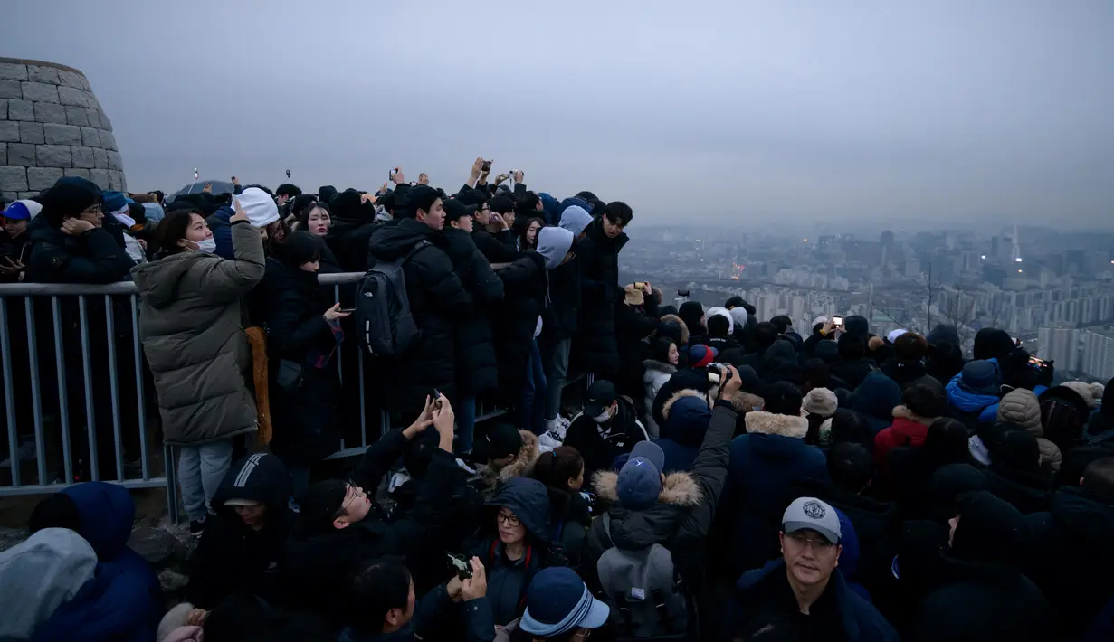 Orang-orang berkumpul di sudut pandang yang menghadap ke cakrawala kota untuk menyaksikan matahari terbit pertama tahun baru, meskipun dalam kondisi mendung, di Seoul, Korea Selatan (1/1/2020). (AFP/Ed Jones)