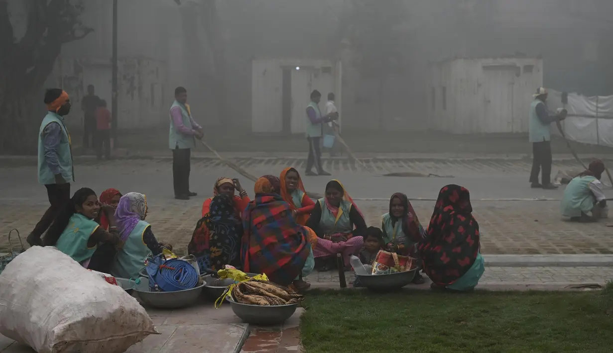 Para pekerja berkumpul saat mereka membersihkan jalan di dekat Gerbang India di tengah kabut asap tebal di New Delhi pada Rabu (22/2/2023). (Arun SANKAR/AFP)