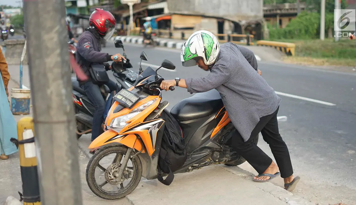 Pengendara mendorong motornya menerobos separator untuk memutar balik di Jalan Raya Pantura, Palimanan, Cirebon, Jawa Barat, Jumat (7/6/2019). Ditutupnya sejumlah jalur putar balik menyebabkan warga nekat menerobos separator untuk memersingkat waktu tempuh. (Liputan6.com/Immanuel Antonius)