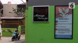 Warga melintas di sebelah papan berisikan poin-poin pancasila di Kampung Pancasila, Karang Tengah, Kota Tangerang, Selasa (1/6/2021). Kegiatan tersebut antara lain seperti gotong royong membersihkan kampung dan sosialisasi penanaman nilai Pancasila kepada warga . (Liputan6.com/Angga Yuniar)