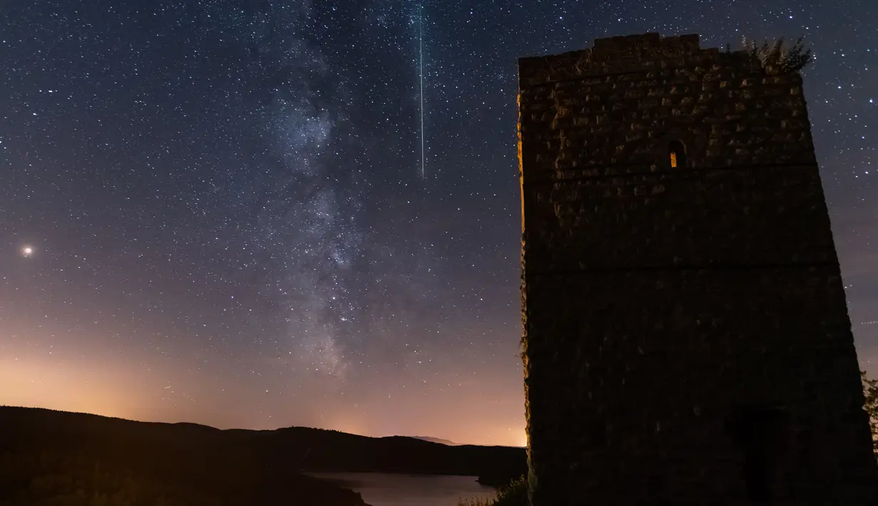 Sebuah meteor melintasi langit malam di sebelah Bima Sakti selama hujan meteor tahunan Perseid di danau Pierre-Percee, Perancis timur, Minggu (12/8). Puncak hujan meteor terjadi pada 11-12 Agustus dan 12-13 Agustus. (Patrick HERTZOG / AFP)