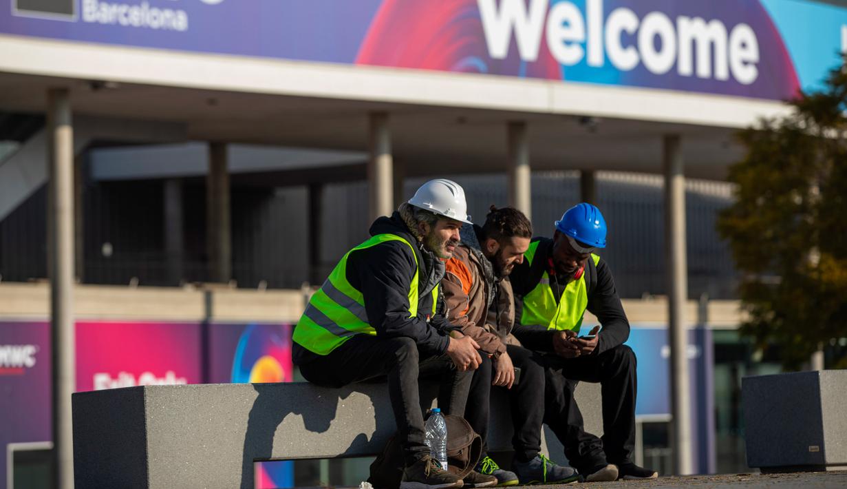 Para pekerja Mobile World Congress (MWC) 2020 duduk di luar lokasi pameran di Barcelona, Spanyol, Kamis (13/2/2020). Penyelenggara MWC 2020, GSMA, batal menggelar pameran telekomunikasi terbesar di dunia tersebut karena ancaman virus corona. (AP Photo/Emilio Morenatti)
