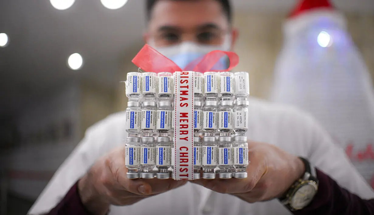 Anggota staf medis di pusat vaksinasi COVID-19 memegang kotak hadiah yang terbuat dari botol vaksin kosong di Bucharest, Rumania, 6 Desember 2021. Pusat vaksinasi COVID-19 membangun pohon Natal setinggi tiga meter dari 19 ribu botol vaksin COVID-19 kosong. (AP Photo/Andreea Alexandru)