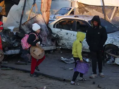 Anak-anak Palestina membawa barang-barang yang dapat diselamatkan berjalan di tengah kehancuran yang disebabkan oleh serangan Israel terhadap kamp pengungsian sementara di Mawasi Khan Yunis, Jalur Gaza selatan pada tanggal 2 Januari 2025. (BASHAR TALEB/AFP)