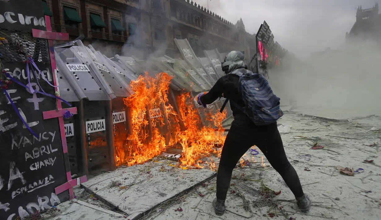 Seorang demonstran melemparkan bensin ke barikade polisi yang melindungi Istana Nasional selama pawai untuk memperingati Hari Perempuan Internasional dan protes terhadap kekerasan gender di Mexico City, Meksiko, Senin (8/3/2021). (AP Photo/Ginnette Riquelme)