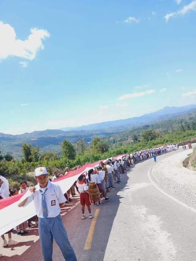 Ratusan warga saat membentangkan bendera raksasa di sepanjang jalan sabuk merah perbatasan RI-Timor Leste (Liputan6.com/Ola Keda)