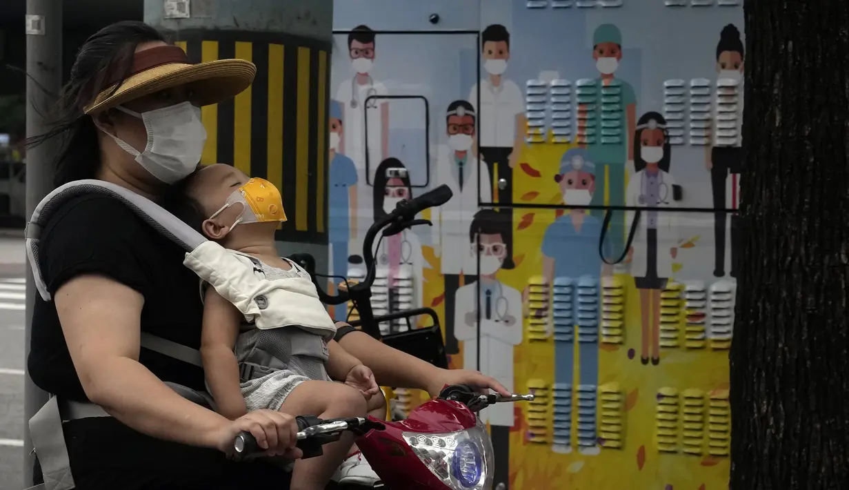 Seorang wanita yang mengenakan masker membawa seorang anak melewati gambar pekerja medis mengenakan masker di Beijing, China, 12 Juli 2022. Beijing telah membatalkan rencana untuk mengizinkan hanya orang yang divaksinasi yang memasuki ruang publik. (AP Photo/Ng Han Guan)