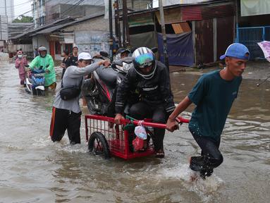 Pengendara sepeda motor menggunakan jasa angkut gerobak saat melintasi banjir yang merendam jalan KH Hasyim Ashari, Kota Tangerang, Banten, Sabtu (16/7/2022). Warga sekitar membantu para pengendara yang melintas agar tidak terkena banjir dengan menawarkan jasa gerobak. (Liputan6.com/Angga Yuniar)