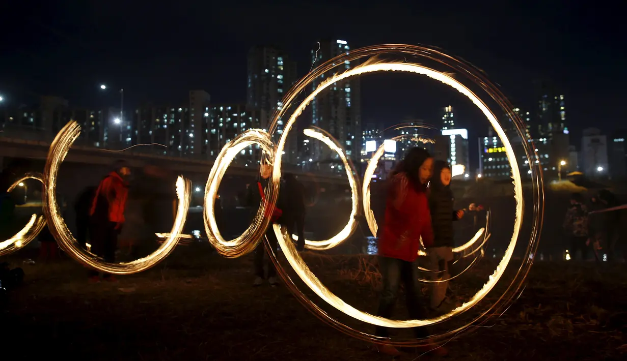 Sejumlah anak memutarkan kaleng berisi kayu yang dibakar jelang perayaan "Jeongwol Daeboreum"di sebuah taman di Seoul, Korea Selatan, Minggu (21/2). Tarian api ini merupakan bagian dari perayaan Imlek ala Korea. (REUTERS/Kim Hong-Ji)