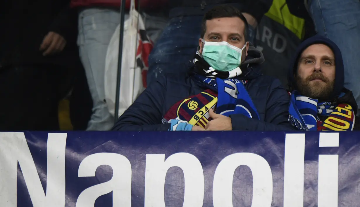 Seorang suporter Napoli  mengenakan masker menunggu dimulainya pertandingan antara Napoli dan Barcelona di Stadion San Paolo di Naples, Italia, Selasa, (25/2/2020). Dalam laga ini, Barcelona berhasil menanhan tuan rumah Napoli 1-1. (AFP Photo/Filippo Monteforte)