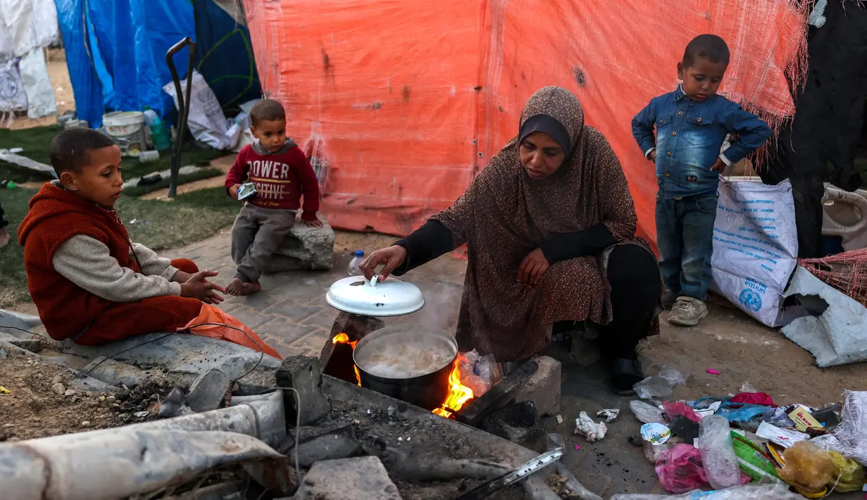 Seorang wanita memasak di sebuah kamp untuk pengungsi Palestina di Khan Yunis, di Jalur Gaza selatan pada 29 Desember 2024. (BASHAR TALEB/AFP)