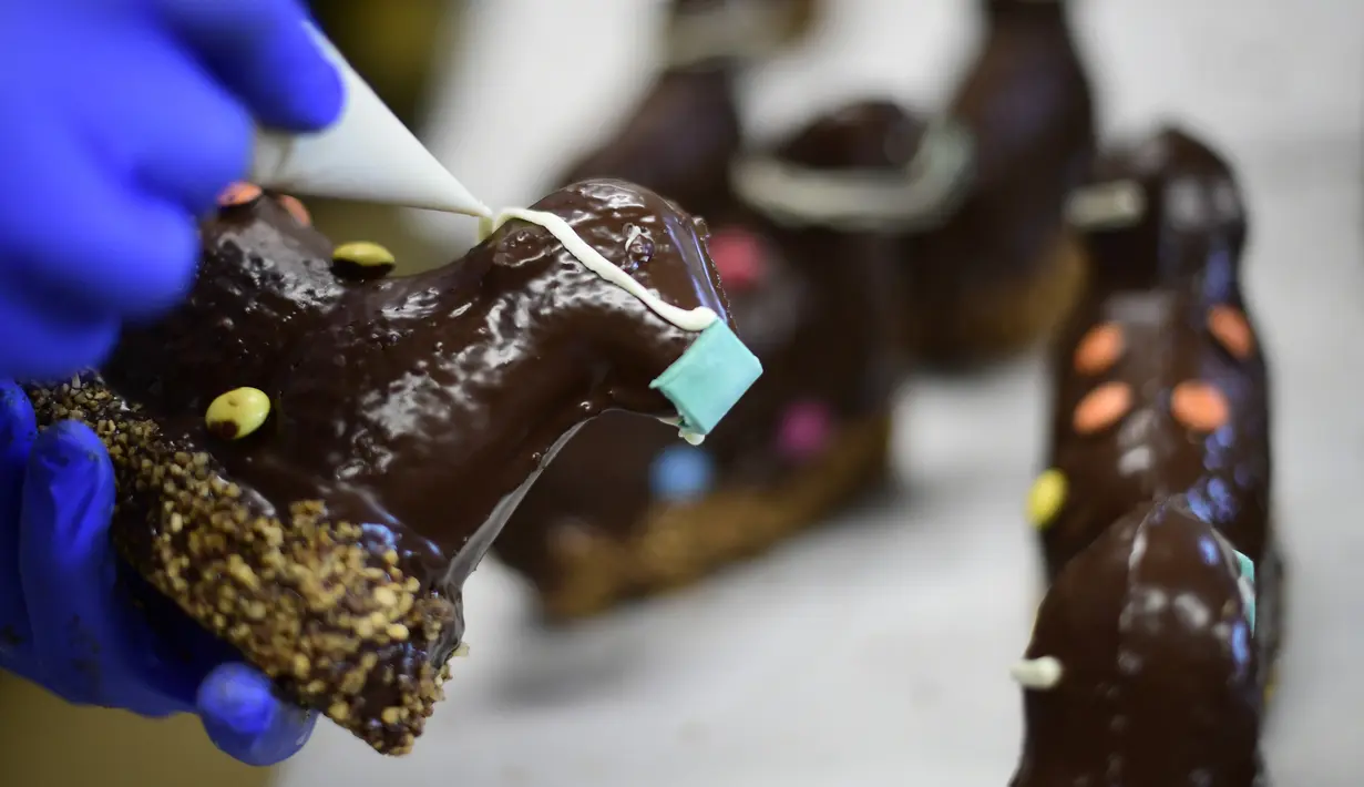 Pembuat roti menghias kue cokelat Paskah berbentuk domba tradisional dengan masker di toko roti Schuerener Backparadies, Dortmund, Jerman, Rabu (8/4/2020). Pembuatan kue Paskah dengan masker bertepatan dengan pandemi virus corona COVID-19. (Ina FASSBENDER/AFP)