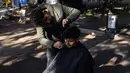 Mohammed al-Hamo (kiri) memotong rambut saudara laki-lakinya, Sobhi di depan tenda mereka di kamp darurat pengungsi korban gempa Turki dan Suriah di kota Antakya pada 19 Februari 2023. Mohammed al-Hamo tak pernah membayangkan akan menggunakan keterampilannya mencukur rambut akan digunakan di tenda pengungsi korban gempa Turki dan Suriah. (Sameer Al-DOUMY / AFP)
