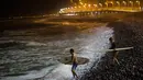 Dua peselancar berjalan di atas bebatuan menuju Samudra Pasifik saat akan berselancar di pantai La Pampilla, ibu kota Peru, Lima, 1 Maret 2017. Sekelompok peselancar hardcore memilih bermain selancar pada malam hari. (AP Photo/Rodrigo Abd)