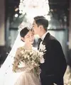 Mengenakan gaun pengantin yang elegan dan tiara mewah, Lee Da In memegang karangan bunga dan tersenyum cerah, sementara suaminya Lee Seung Gi, mengenakan tuksedo di sampingnya, berpose dengan tangan di sakunya dan mencium keningnya. [Foto: IG/byhumanmade]