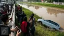 Warga menyaksikan proses evakuasi mobil yang terperosok di saluran Ispeksi Kalimalang, Jabar, Minggu (7/5). Minibus bernopol B 1475 FRK itu tercebur kedalam saluran inspeksi Kalimalang dan sempat terseret arus sejauh 100m. (Liputan6.com/Gempur M Surya)