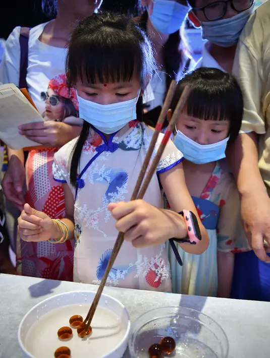 Seorang anak mencoba mengambil kelereng dengan sumpit dalam acara perayaan Festival Pertengahan Musim Gugur di Museum Hainan, Haikou, ibu kota Provinsi Hainan, China selatan (1/10/2020). (Xinhua/Guo Cheng)