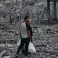 Seorang pria Palestina yang membawa kantong plastik belanja berbicara dengan seorang wanita ketika mereka berdiri di tengah puing-puing setelah serangan udara Israel di lingkungan al-Rimal, Kota Gaza, pada 10 Oktober 2023. (MOHAMMED ABED/AFP)