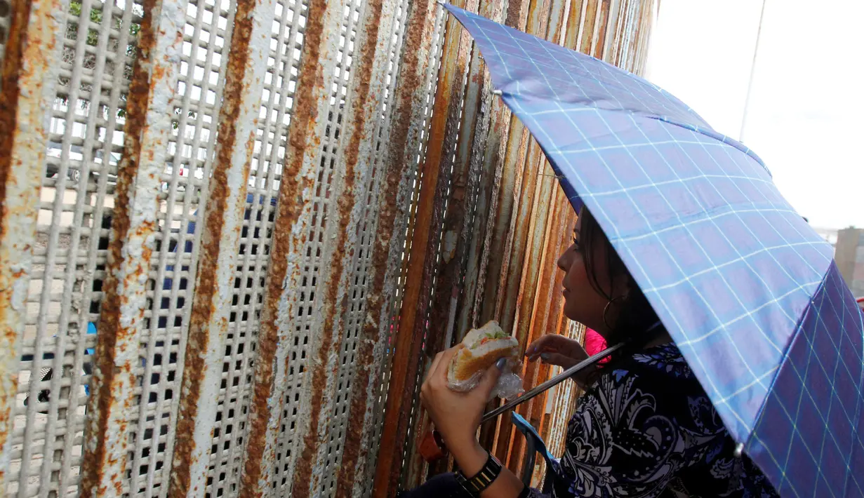Seorang wanita berbincang dengan keluarga mereka di pagar perbatasan antara Meksiko dan Amerika Serikat, Tijuana, Meksiko (19/11). Pagar besar ini memisahkan antara Meksiko dan Amerika Serikat. (REUTERS / Jorge Duenes)