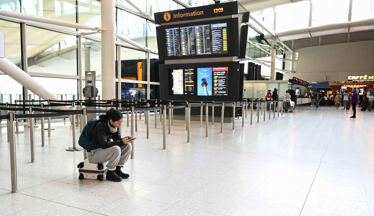 Kondisi ini diberlakukan hingga situasi wilayah udara kembali dinyatakan aman. Tampak dalam foto, seorang penumpang duduk di atas kopernya di bagian kosong area check-in di Bandara Heathrow, London pada Minggu 1 Maret 2026. (JUSTIN TALLIS/AFP)