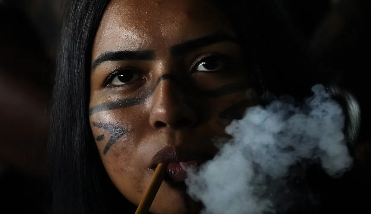 Seorang wanita Pribumi Pataxo merokok pipa tradisional selama upacara yang disebut Pertemuan Masyarakat Pertama di Kamp Adat Tanah Bebas tahunan ke-18 di Brasilia, Brasil (8/4/2022). Acara digelar selama 10 hari. (AP Photo/Eraldo Peres)