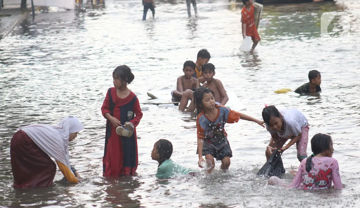 Sejumlah anak-anak bermain di genangan air akibat banjir rob di kawasan pintu masuk Pelabuhan Nizam Zachman, Muara Baru, Jakarta, Jumat (5/6/2020). Banjir rob di Pelabuhan Muara Baru tersebut terjadi akibat cuaca ekstrem serta pasang air laut. (Liputan6.com/Helmi Fithriansyah)