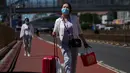 Seorang wanita mengenakan masker berjalan dengan barang bawaannya di jalan saat dia meninggalkan stasiun kereta api Beijing di Beijing, Selasa (6/9/2022). China lockdown jutaan warganya di bawah pembatasan ketat COVID-19 dan melarang warganya lakukan perjalanan domestik pada hari libur nasional yang akan datang. (AP Photo/Andy Wong)