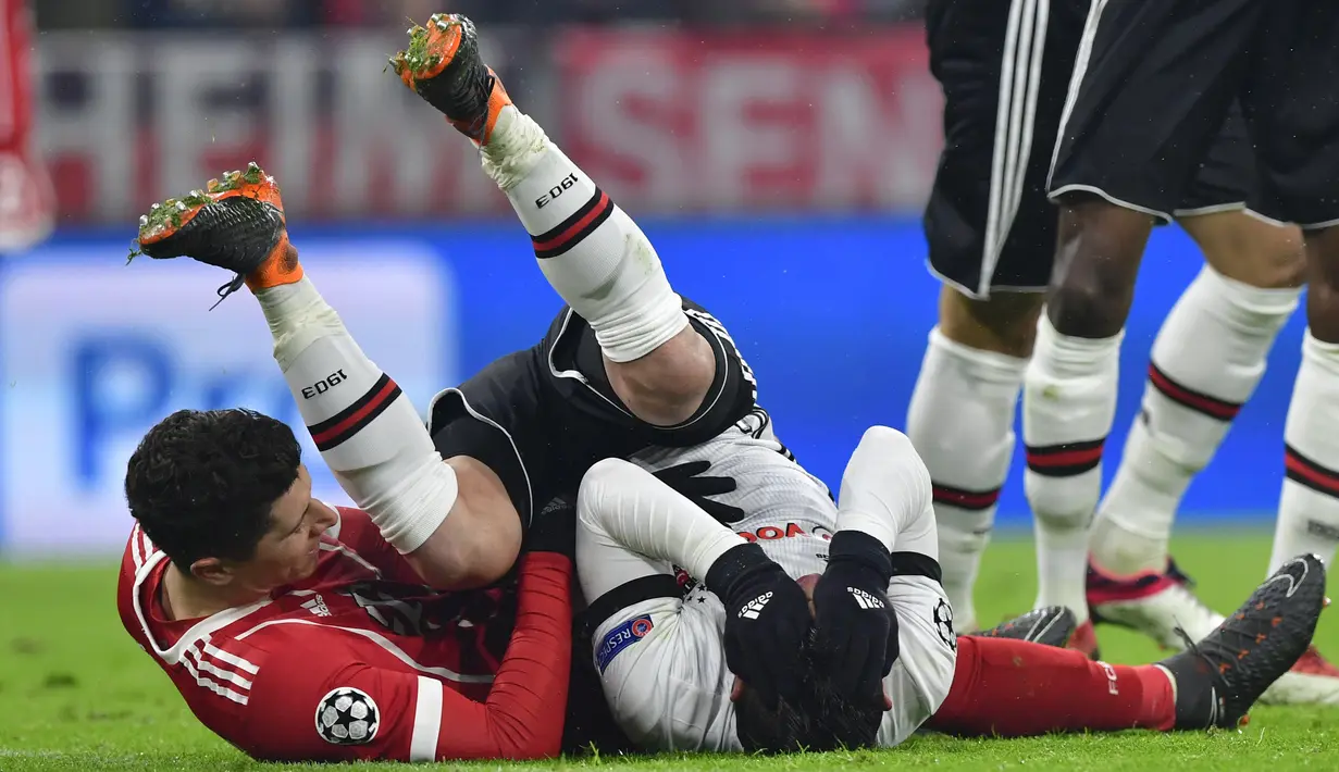 Bek Besiktas, Gary Alexis Medel Soto dan pemain Bayern Munchen, Robert Lewandowski terjatuh saat berebut bola pada pertandingan pertama babak 16 besar Liga Champions di Allianz Arena, Selasa (20/2). Bayern menang telak dengan skor 5-0 (Thomas KIENZLE/AFP)