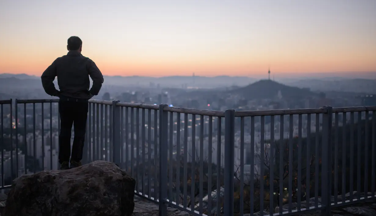 Seorang pejalan kaki melihat pemandangan kota Seoul dan menara Namsan selama matahari terbit di Korea Selatan (31/10). Kota ini adalah pusat politik, budaya, sosial dan ekonomi di Korea Selatan dan Asia Timur. (AFP Photo/Ed Jones)