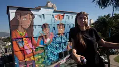 Seniman Brasil, Luna Buschinelli berpose dengan latar belakang mural berjudul 'Contos' di dinding gedung sekolah Rio de Janeiro, (19/6). Karya gadis 19 tahun itu memecahkan rekor dunia sebagai mural terbesar yang dibuat oleh wanita. (AP/Silvia Izquierdo)