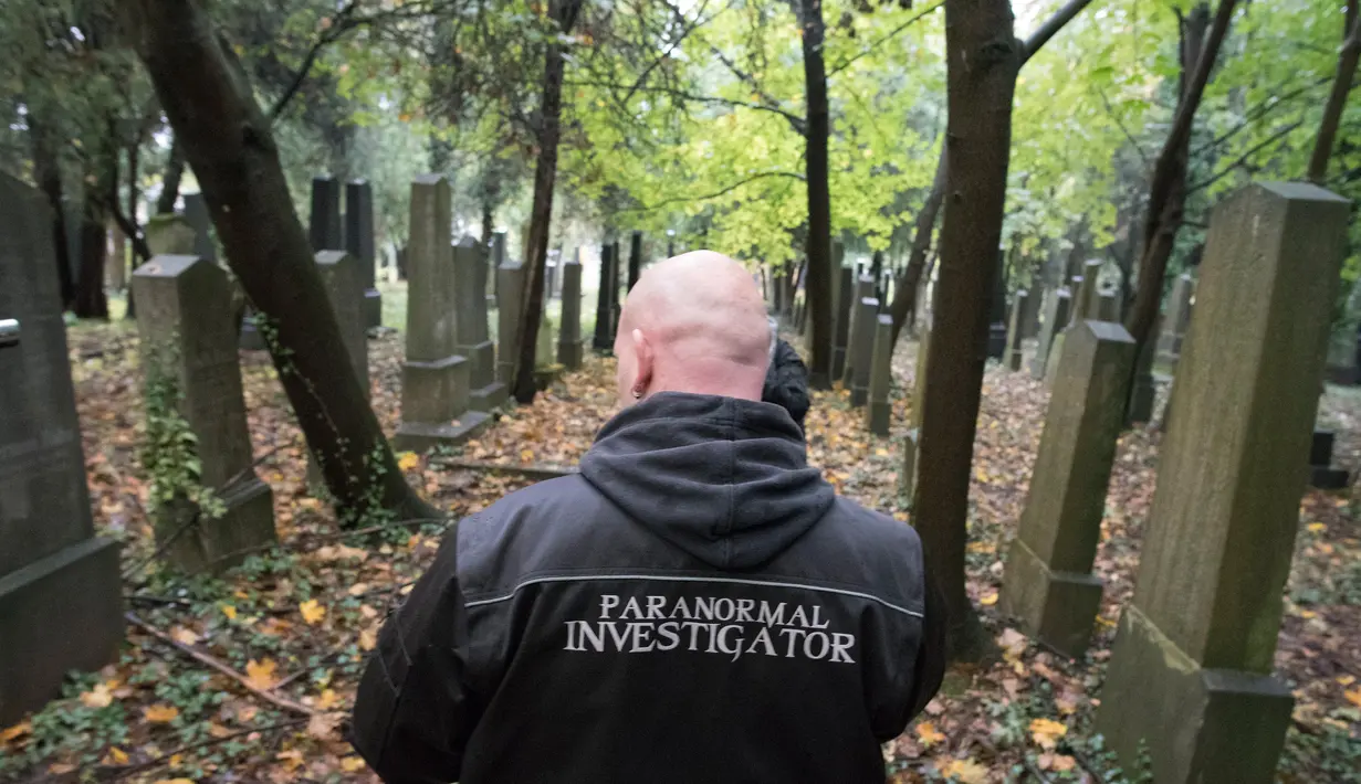 Aksi seorang pemburu hantu menelusuri batu nisan untuk mencari aktivitas gaib di pusat pemakaman tua di Wina, Austria, 20 Oktober 2016. Pemakaman ini disinyalir memiliki aura mistis yang kental dengan aktivitas makhluk halus. (JOE KLAMAR/AFP)