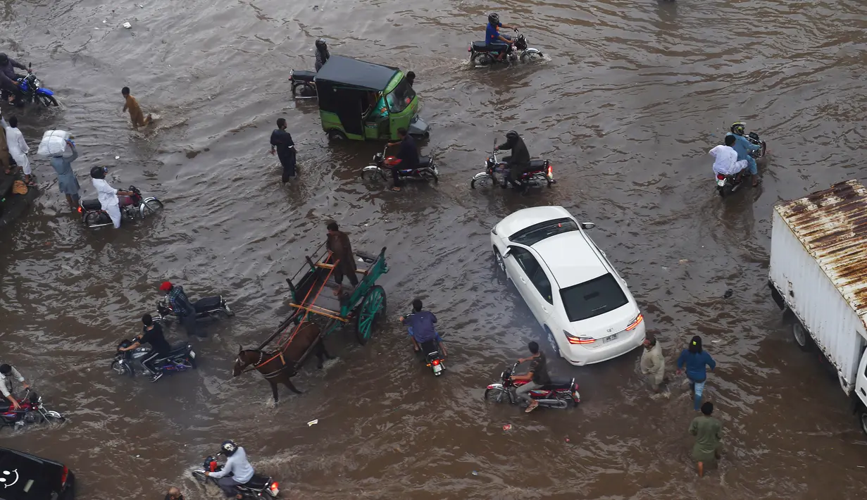 Sejumlah warga melintasi banjir saat beraktivitas setelah hujan deras di Lahore, Pakistan (16/7/2019). Di Kashmir yang dikelola Pakistan, para pejabat pemerintah mengatakan sedikitnya 23 orang tewas setelah hujan lebat memicu banjir bandang. (AFP Photo/Arif Ali)