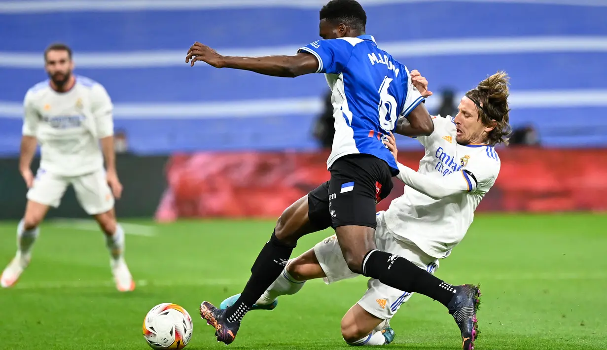 Gelandang Deportivo Alaves Mamadou Loum berebut bola dengan gelandang Real Madrid Luka Modric pada pekan ke-25 La Liga Spanyol di Santiago Bernabeu, Minggu (20/2/2022) dinihari WIB. Real Madrid menang meyakinkan dengan skor 3-0. (OSCAR DEL POZO / AFP)
