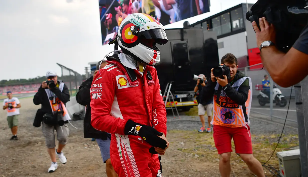 Sebastian Vettel berjalan menuju pit stop setelah mengalami kecelakaan pada balapan F1 Grand Prix di Hockenheim racing circuit, Jerman, (22/7/2018). Vettel kehilangan kendali saat perubahan cuaca dan menabrak pembatas. (AFP/ Andrej Isakovic)