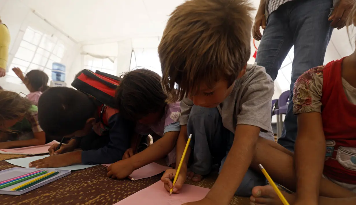 Sejumlah anak pengungsi saat mengikuti kegiatan belajar di sebuah kamp di Ain Issa, Suriah (22/8). Meski belajar di dalam tenda pengungsian, anak-anak tetap antusias mengikuti hari pertama tahun ajaran baru sekolah. (AFP Photo/Delil souleiman)