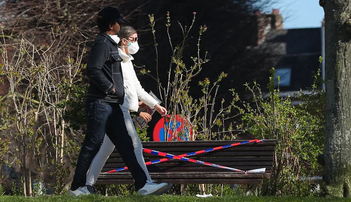 Orang-orang berjalan melewati bangku yang dipasangi garis polisi di Brussel, Belgia, pada 25 Maret 2020. Deretan bangku di sejumlah taman dilarang diduduki untuk mencegah orang-orang berkumpul atau berada terlalu lama di area publik tersebut. (Xinhua/Zheng Huansong)