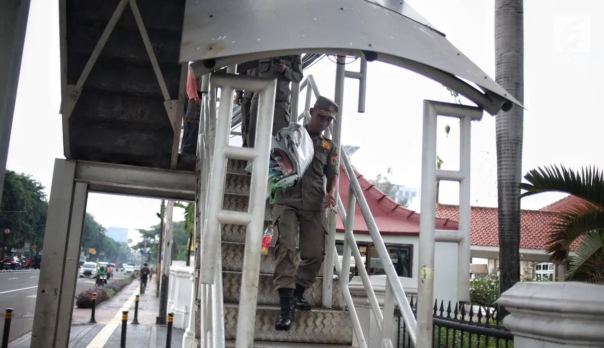 Petugas Satpol PP mencopot alat peraga kampanye (APK) berupa spanduk caleg di JPO kawasan Gambir, Jakarta, Sabtu  (22/12). PenertiBan spanduk APK dilakukan karena melanggar aturan pemasangan dari komisi pemilihan umum. (Liputan6.com/Faizal Fanani)