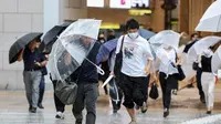 Pejalan kaki mencoba berlindung dari angin dan hujan saat mereka menyeberang jalan di depan Stasiun Osaka pada 15 Agustus 2023, saat Badai Tropis Lan menerjang pulau utama Honshu pada malam hari. (Dok:&nbsp;STR / JIJI Press / AFP)