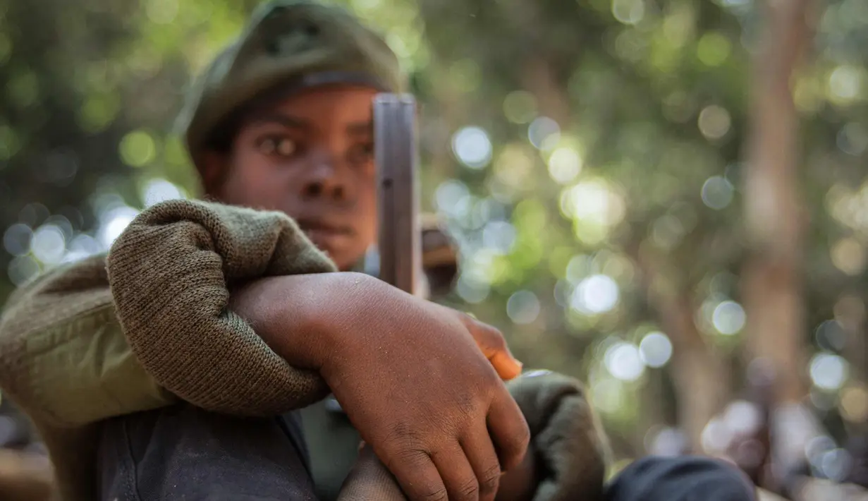 Tentara anak yang baru dibebaskan duduk dengan senapan pada sebuah upacara di Yambio, Sudan Selatan, (7/2). Konflik ini menyebabkan puluhan ribu orang kehilangan nyawa. (AFP PHOTO/Stefanie Glinski)