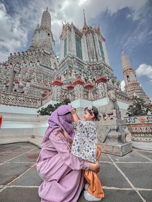Berkunjung ke candi Buddha terkenal di Thailand, Wat Arun, Ria Ricis dan Moana tampil serasi pakai outfit warna pastel. Ria Ricis dengan gamis ungu, sementara Moana dengan floral top warna ungu senada. [@riaricis1795]
