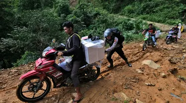 Seorang petugas polisi membantu petugas pemilu mendorong sepeda motor mendaki bukit saat mendistribusikan kotak suara dan perlengkapan pemilu lainnya ke tempat pemungutan suara (TPS) di desa-desa terpencil di Maros, Sulawesi Selatan, Selasa, 13 Februari 2024. (AP Photo/Masyudi S. Firmansyah)