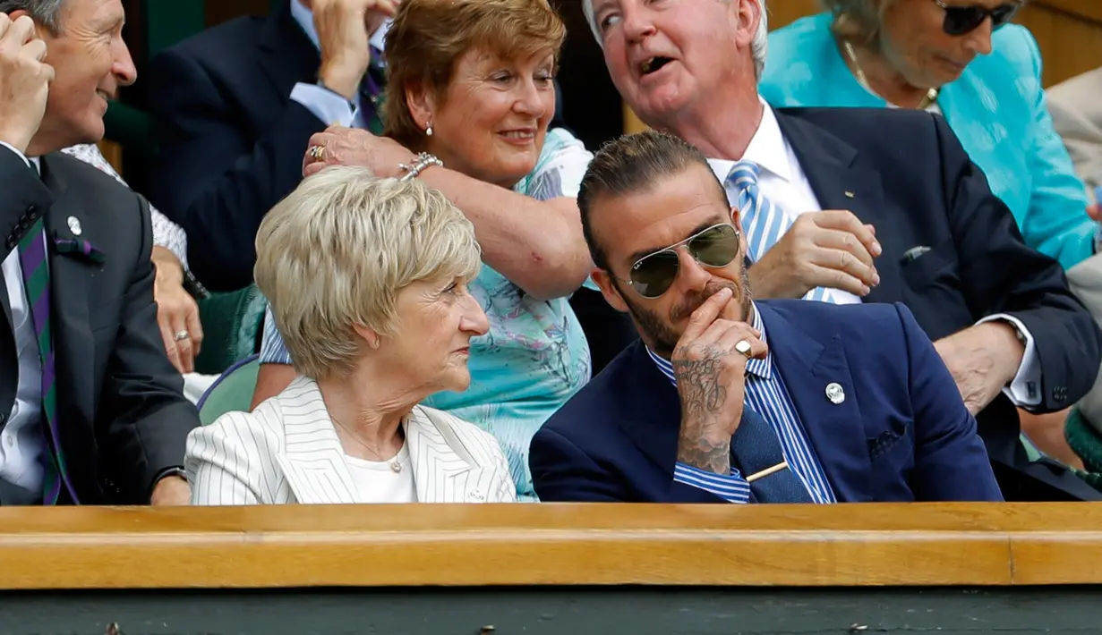 Aktor David Beckham berbincang dengan ibunya Sandra menyaksikan dari Royal Box pada hari kelima di Kejuaraan Tenis Wimbledon 2017 di London, Inggris (7/7). Beckham tampil dengan jas berwarna biru dan menggunakan kaca mata hitam. (AP Photo/Alastair Grant)