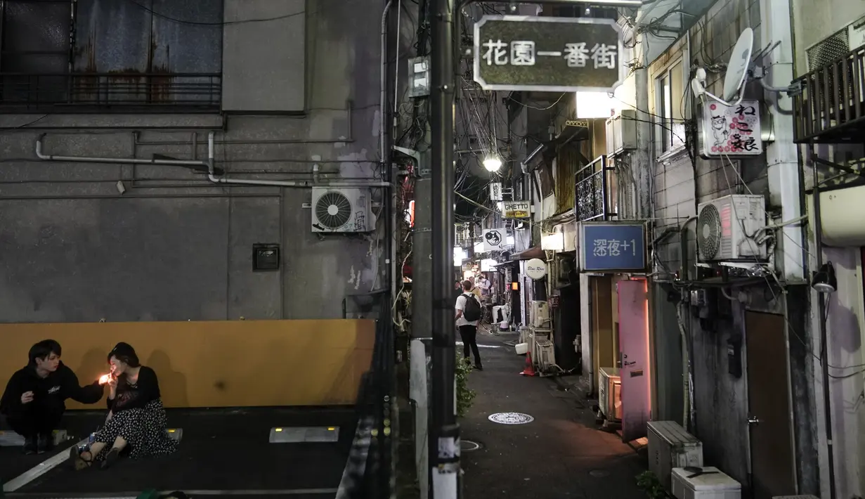Suami-istri merokok di tempat parkir yang berdekatan dengan Golden Gai di distrik Shinjuku, Tokyo (28/7/2019). Shinjuku Golden Gai adalah daerah kecil di Kabukicho, Shinjuku, Tokyo, Jepang, yang terkenal baik sebagai bidang minat arsitektur dan kehidupan malamnya. (AFP Photo/Jae C. Hong)