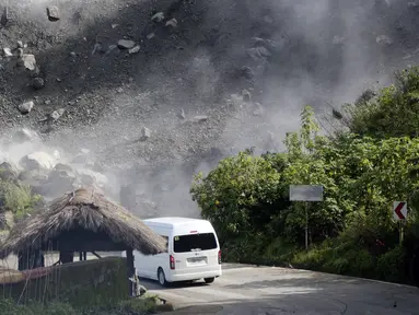 Batu-batu besar berjatuhan saat kendaraan melewati jalan selama gempa bumi di Bauko, Provinsi Mountain, Filipina, 27 Juli 2022. Gempa bumi kuat memicu tanah longsor dan merusak bangunan di Filipina. (AP Photo/Harley Palangchao)