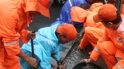 Petugas Penanganan Prasarana dan Sarana Umum (PPSU) membersihkan saluran air di kawasan Gelora Bung Karno, Jakarta, Selasa (17/12/2019). Petugas PPSU membersikan saluran air saat terjadi genangan usai hujan deras mengguyur Jakarta. (Liputan6.com/Herman Zakharia)